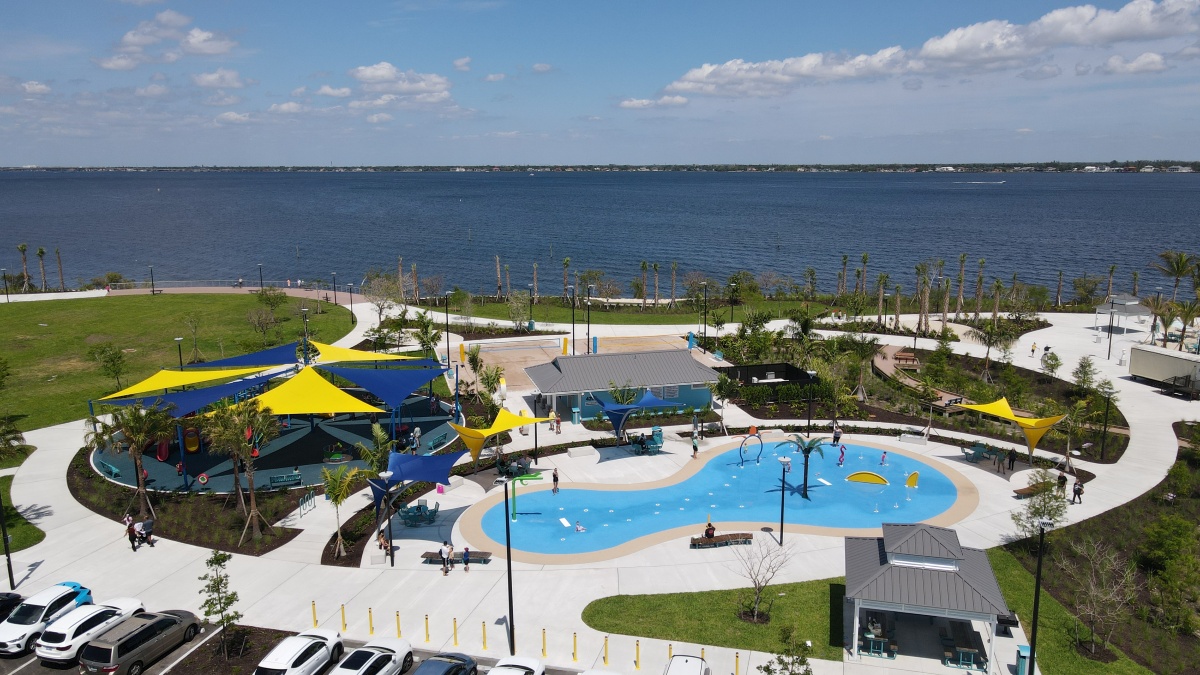 High-angle view of Jaycee Park splash pad, colorful shade sails, and winding walkways surrounded by landscaped gardens.